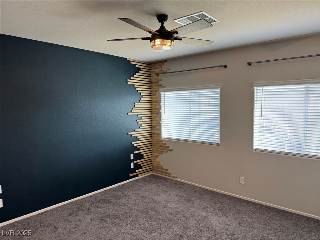 Empty bedroom with a dark blue accent wall, decorative wood slats, two blinded windows, and a ceiling fan.