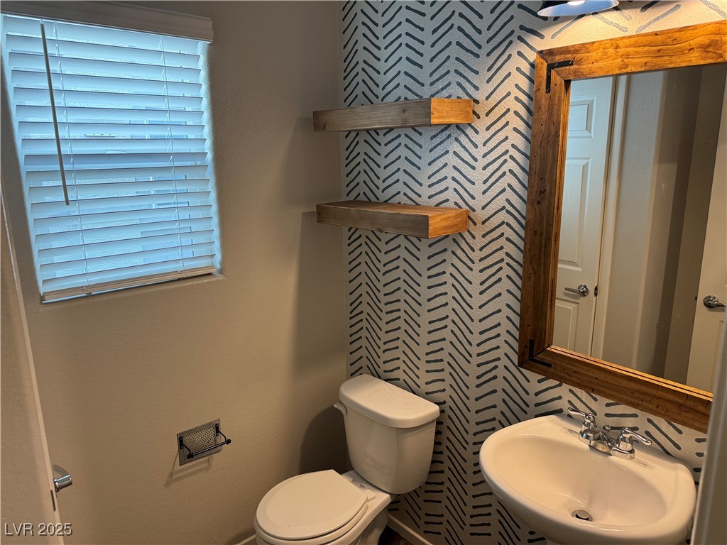Bathroom with a patterned accent wall, wooden shelves, and a rustic wood-framed mirror.