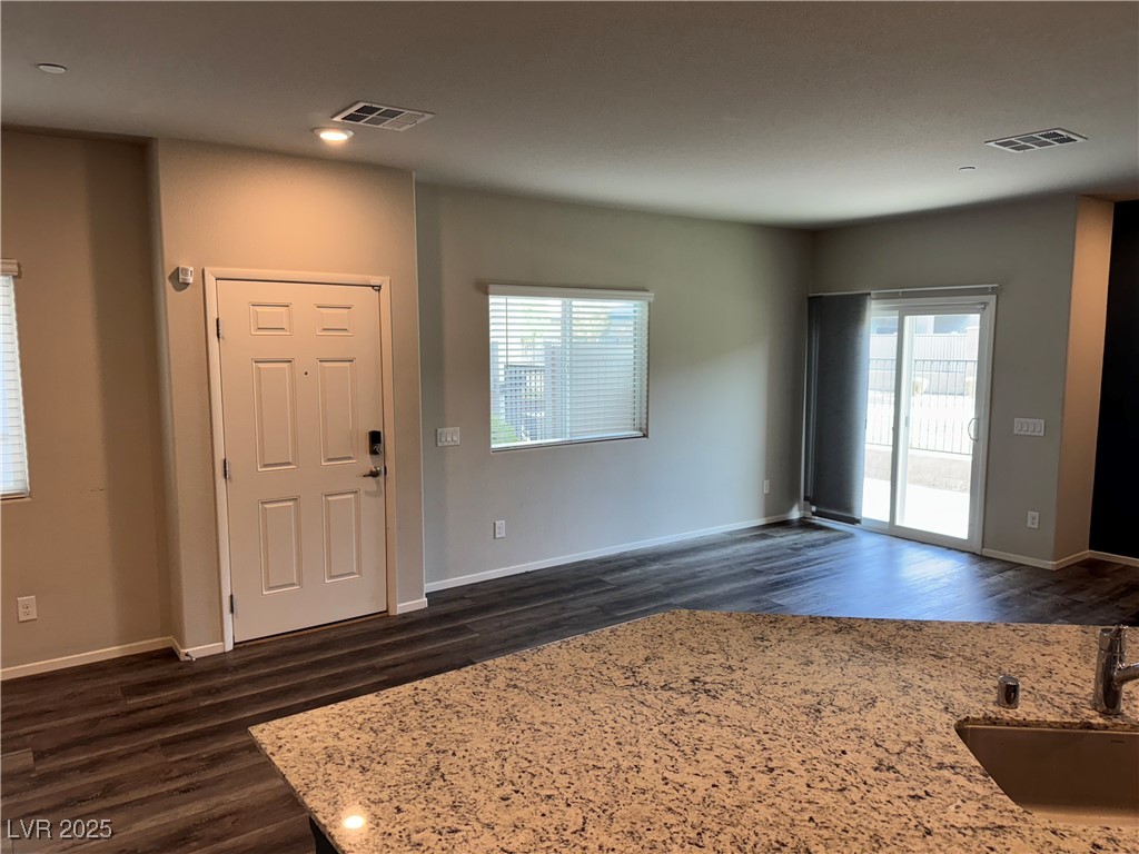 Kitchen and living area with granite countertop, dark flooring, entry door, and sliding glass doors.