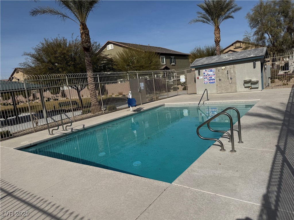 Community swimming pool with metal handrails, a fenced deck, and palm trees.