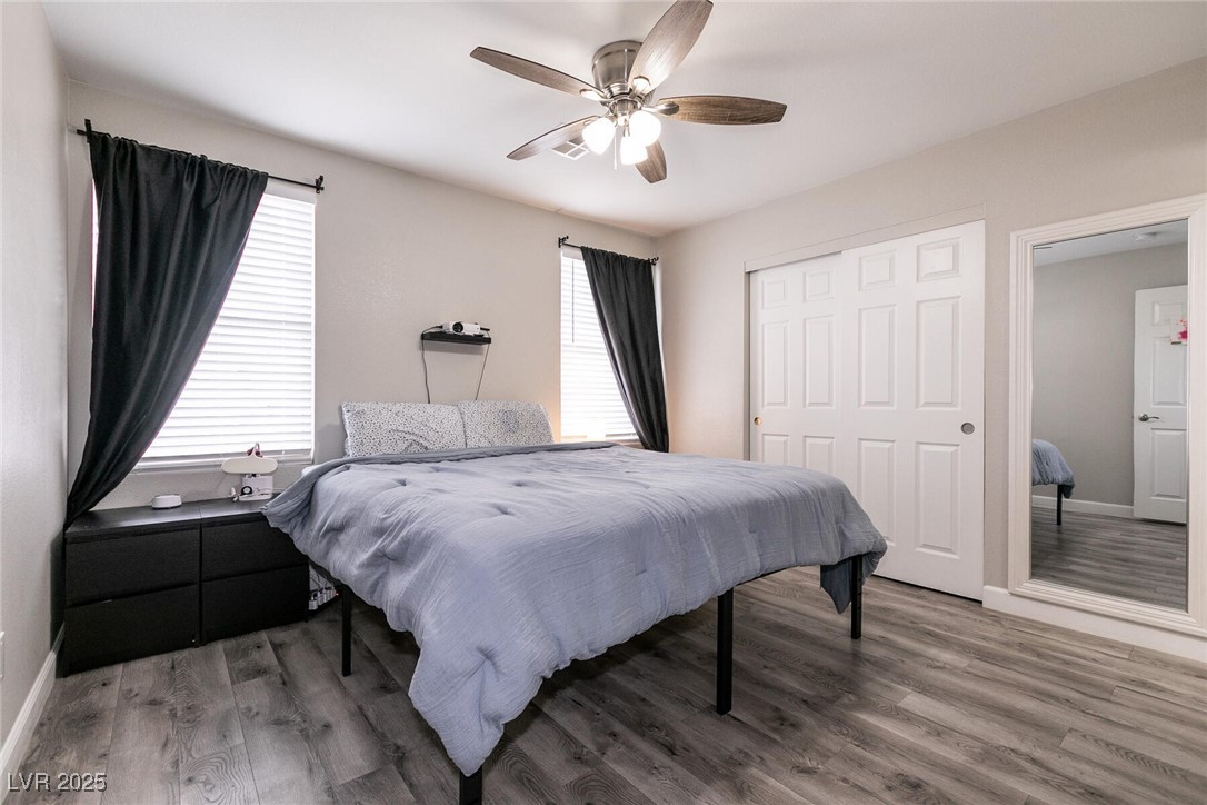 Furnished bedroom with a large gray bed, dark curtains, mirrored closet doors, and a ceiling fan.