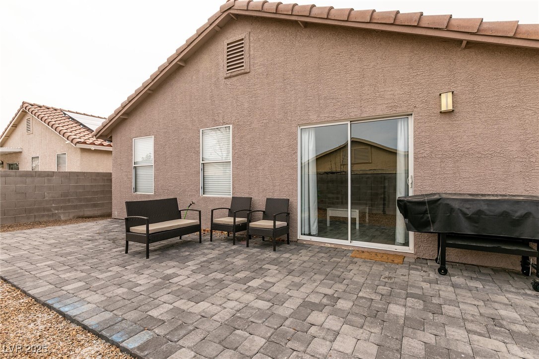 Back patio with gray pavers, wicker seating, and a covered grill beside the sliding glass door.