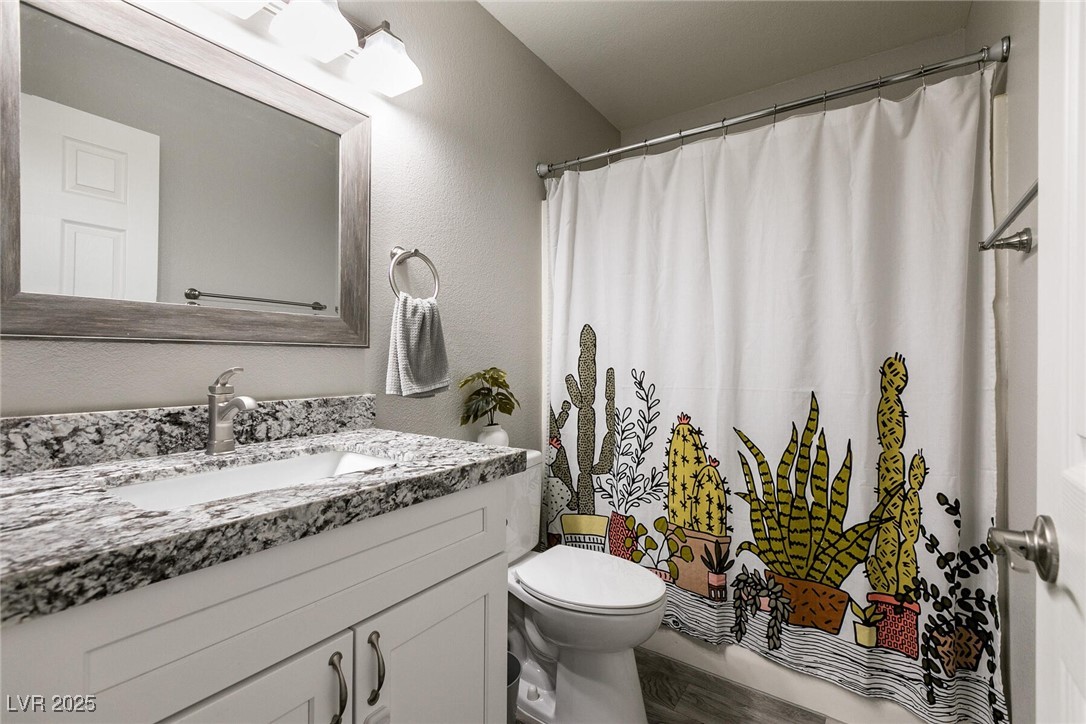 Bathroom with a granite vanity, framed mirror, and colorful cactus-print shower curtain.