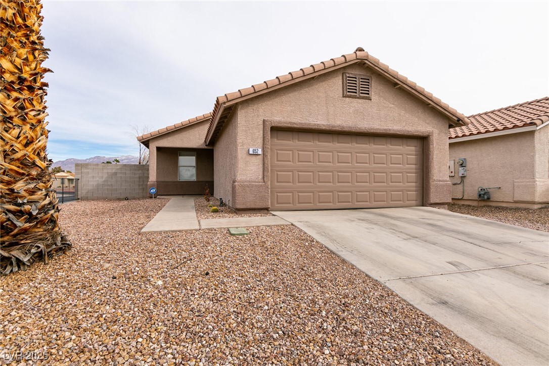 Tan stucco home with a two-car garage, concrete driveway, and rock-covered front yard.