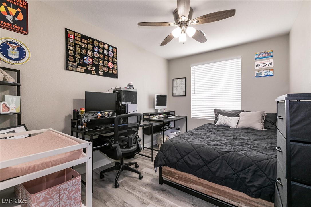 Bedroom with black quilted bed, computer workstation, ceiling fan, and a small white child’s bed.