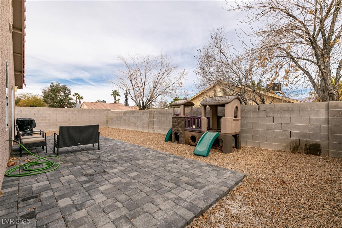 Backyard patio with gray pavers, outdoor chairs, gravel landscaping, and a children's playset.
