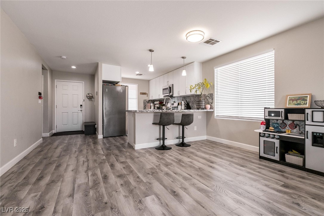 Open living and kitchen area with gray flooring, white cabinets, and a breakfast bar with two stools.