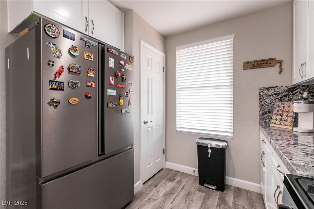 Kitchen with a magnet-covered stainless steel refrigerator, white cabinets, and patterned stone countertops.