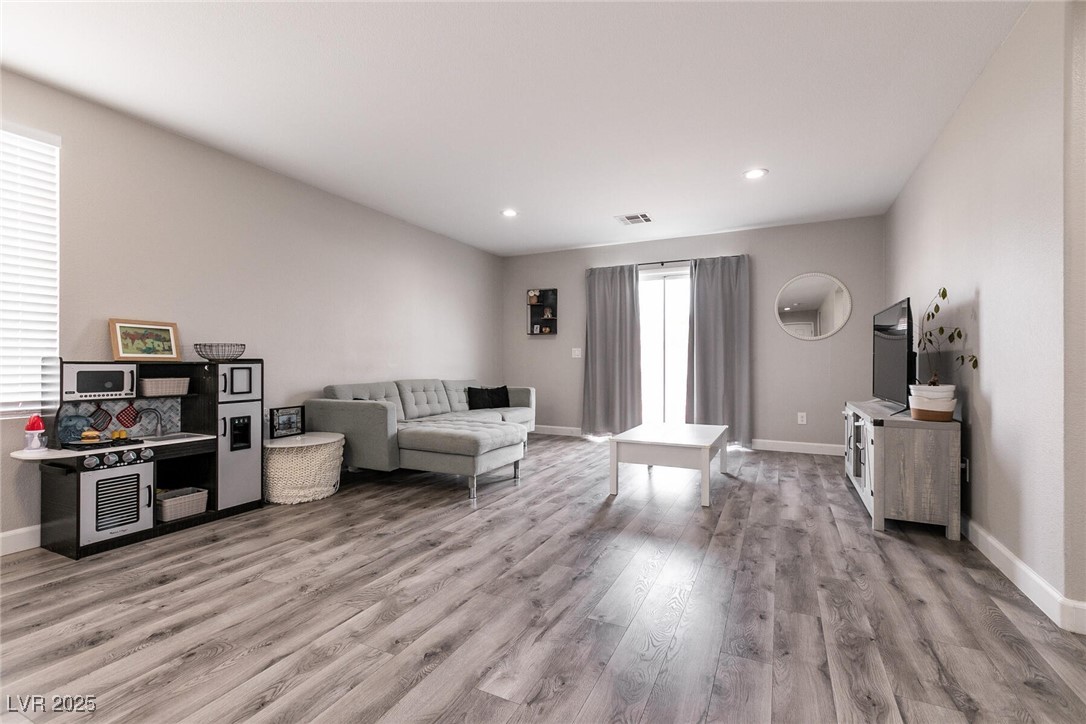 Living room with gray sectional, wood-look floors, and a children’s play kitchen.