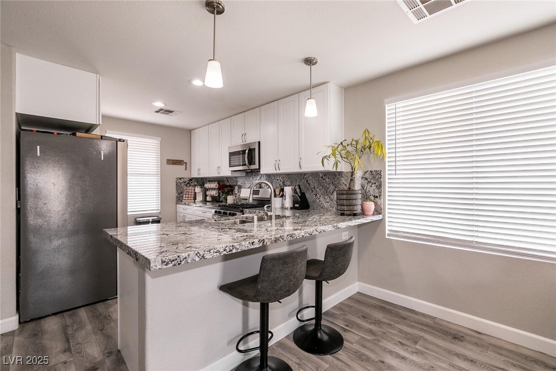 Kitchen with granite breakfast bar, white cabinets, dark refrigerator, and two stools.