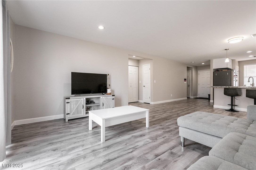 Open-plan living room with gray flooring, a sectional sofa, and a kitchen peninsula with bar stools.
