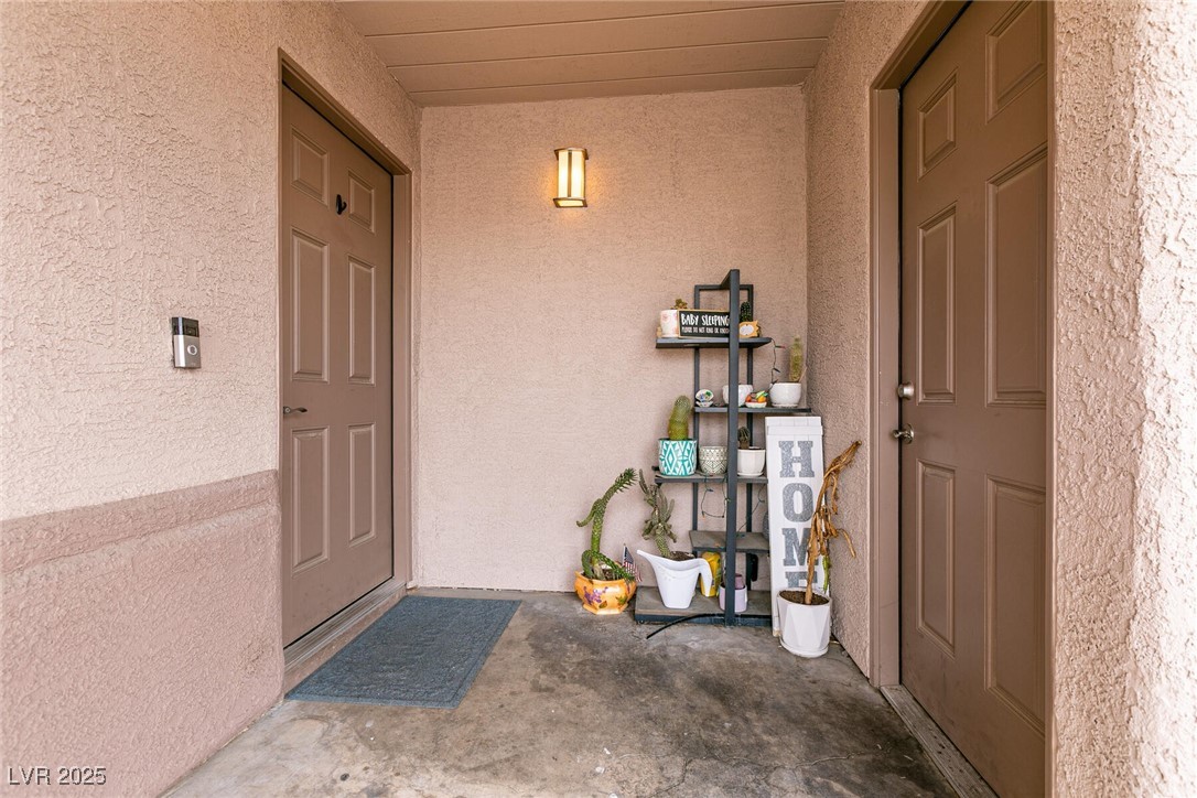 Covered entry with two brown doors, a doormat, and potted plants on a display shelf.