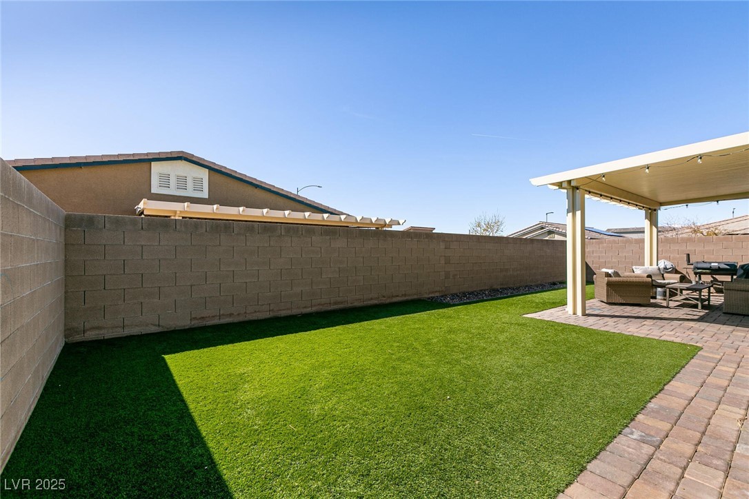 Backyard with artificial turf, paved patio, and covered outdoor seating area.