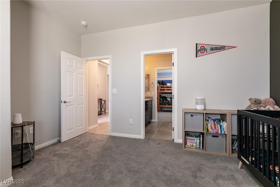 Bedroom nursery with a black crib, children’s bookshelf, gray carpet, and an Ohio State University pennant.