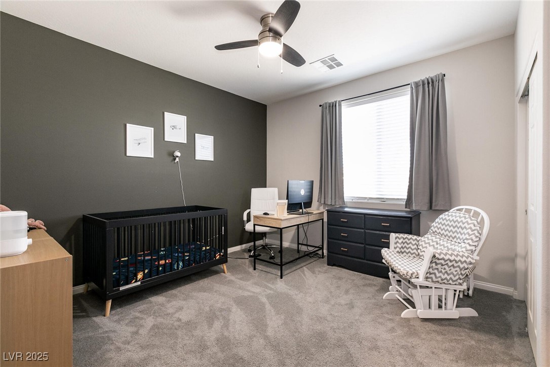 Furnished nursery with a black crib, desk, dresser, and white glider beside a bright window.
