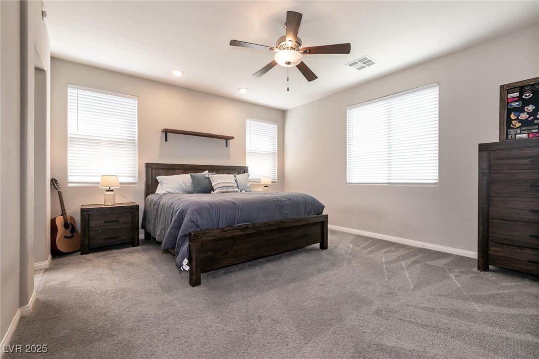 Furnished bedroom with a dark wood bed, gray carpet, three windows, and a ceiling fan.