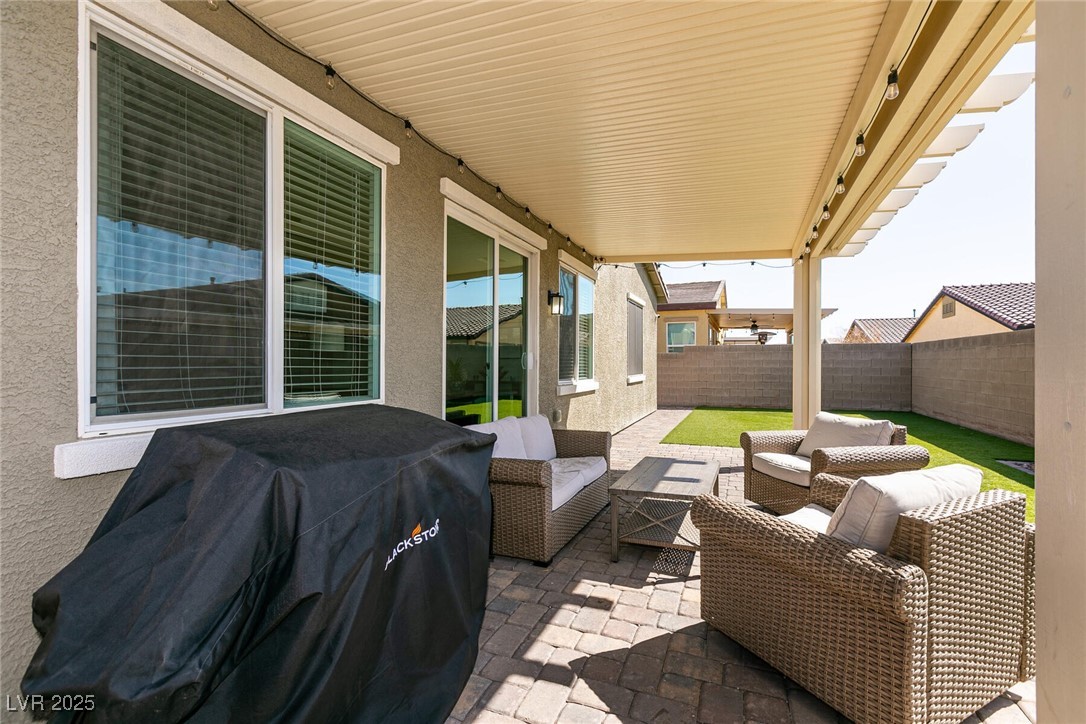 Covered backyard patio with wicker seating, pavers, artificial turf, and a covered grill.