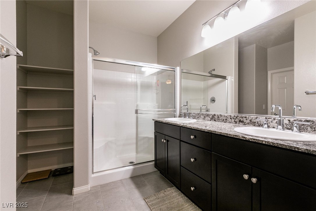 Bathroom with a glass shower, dark double vanity, granite counter, and open shelving.