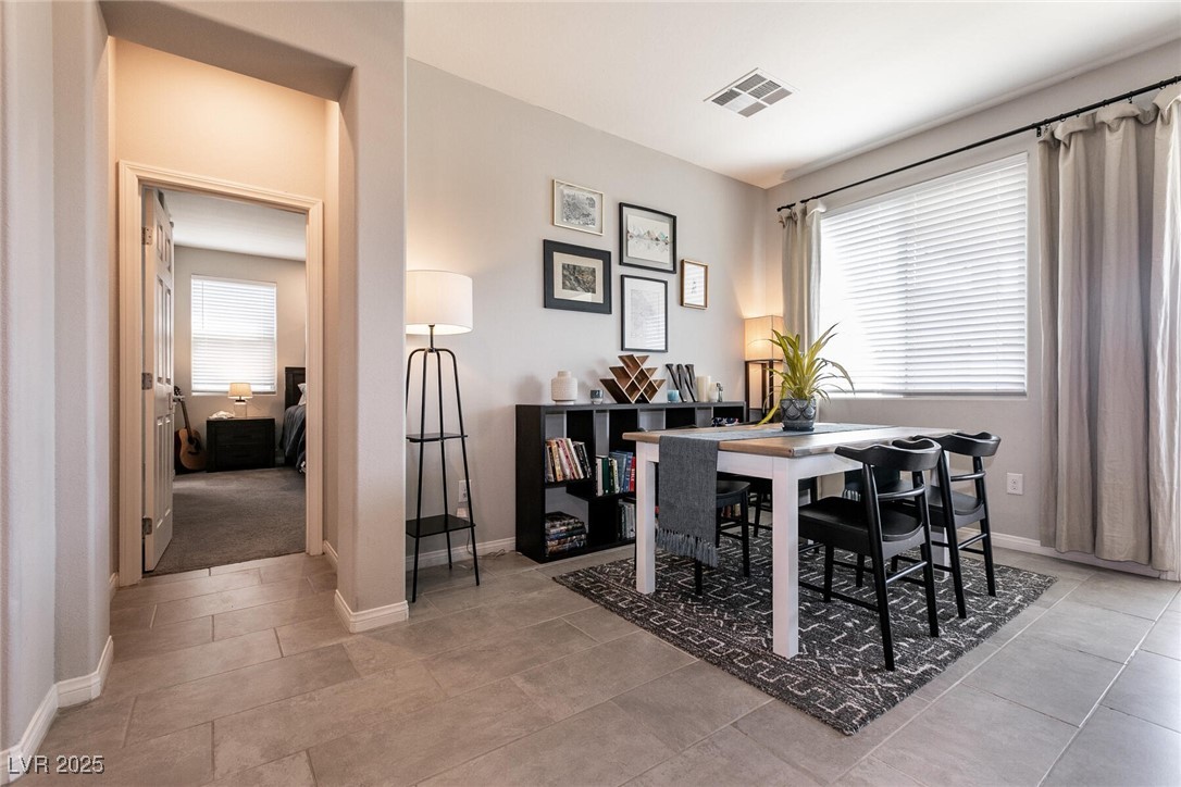 Dining area with a white table, black chairs, patterned rug, and a large curtained window.