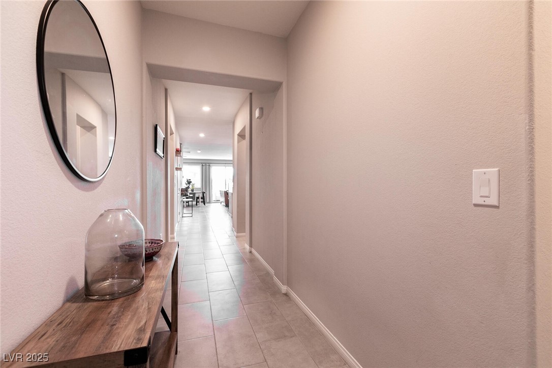 Tiled hallway with a wood console table and round mirror leading to a bright living area.