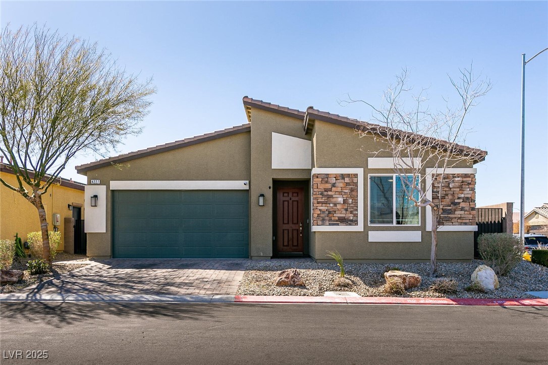 Single-story home with a dark double garage, stone facade accents, and desert landscaping.