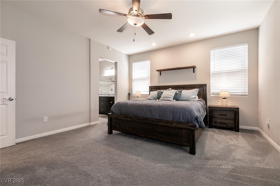 Furnished bedroom with a dark wood bed, gray bedding, ceiling fan, and two windows with white blinds.