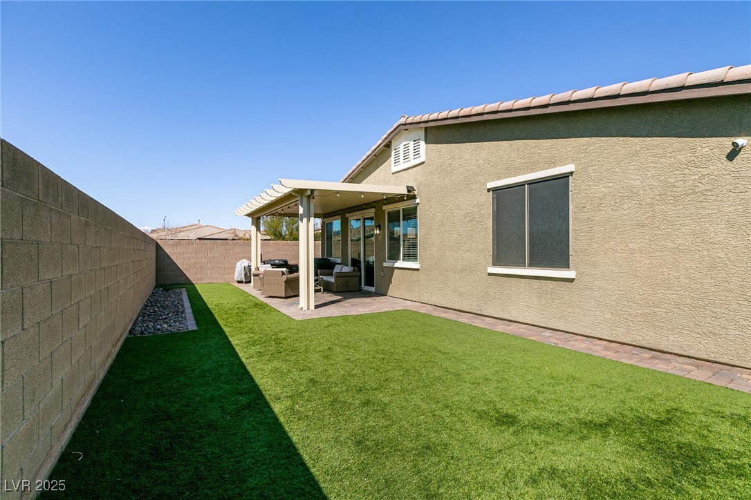 Backyard with green lawn, covered patio, and outdoor seating beside the stucco home.