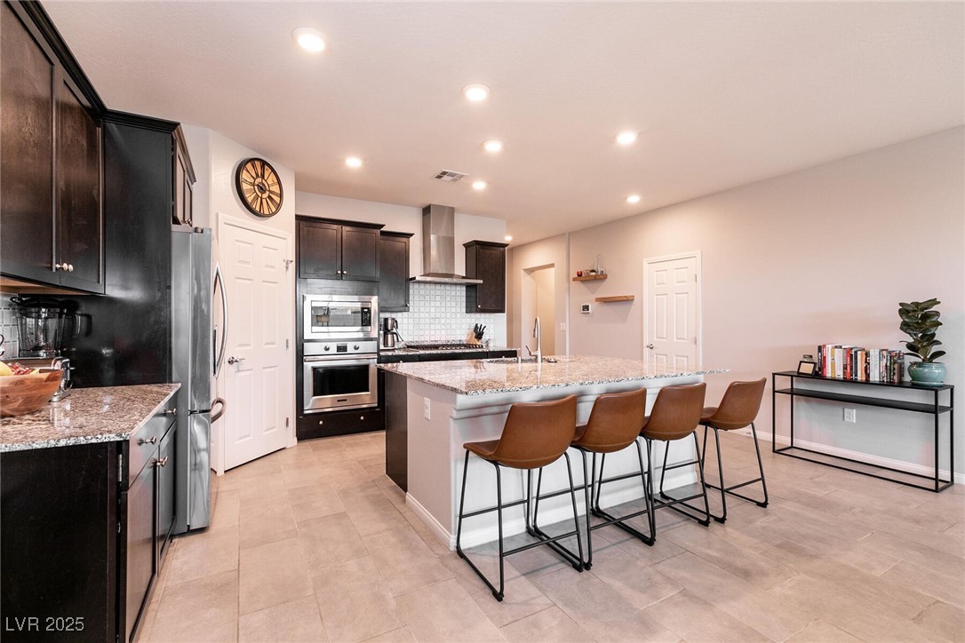 Kitchen with dark cabinets, stainless steel appliances, and a granite island lined with four brown stools.