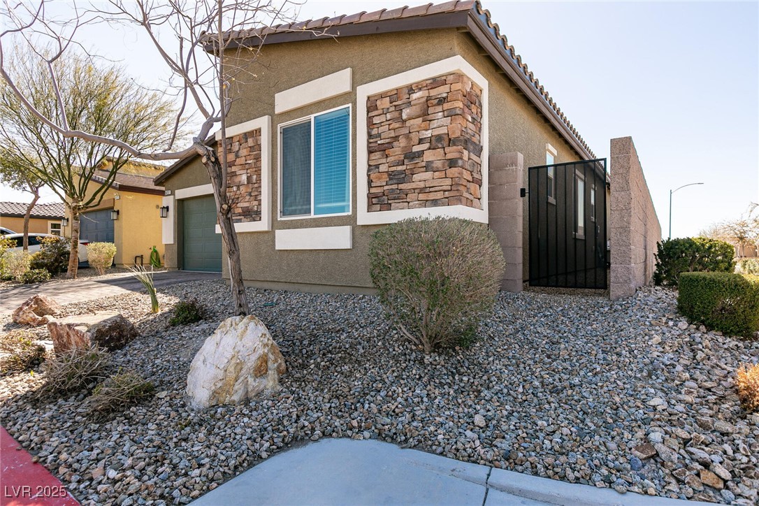 Home exterior with stone accents, a black side gate, and desert rock landscaping.