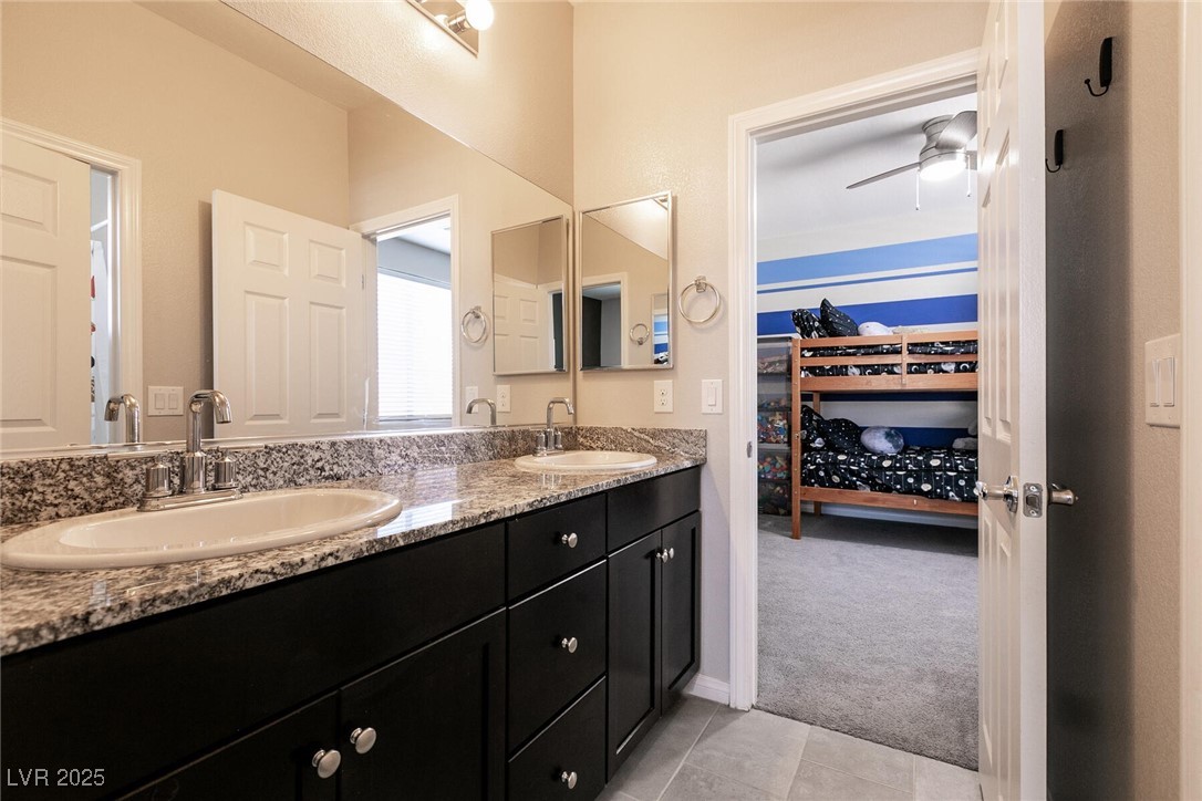 Bathroom vanity with two sinks and granite counter; doorway opens to a bedroom with a bunk bed.
