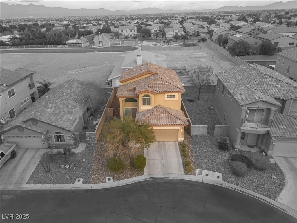 Aerial view of a tan two-story home with a tile roof and gravel landscaping, surrounded by neighboring houses.