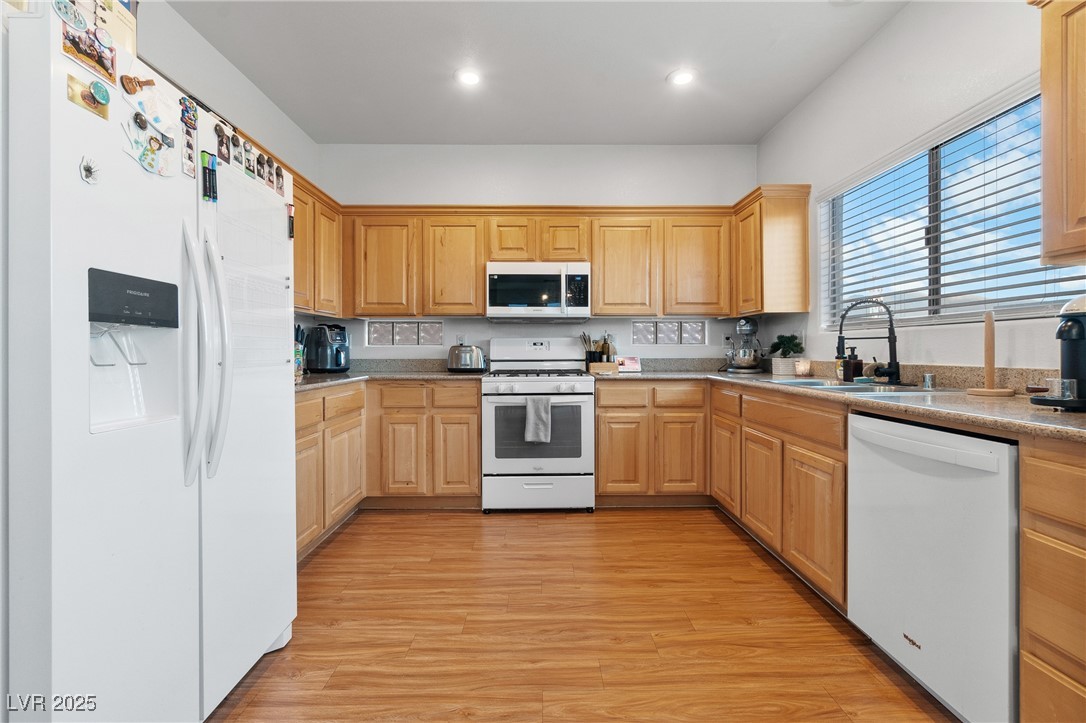 Kitchen with honey-colored cabinets, granite counters, white appliances, and a large window with blinds.