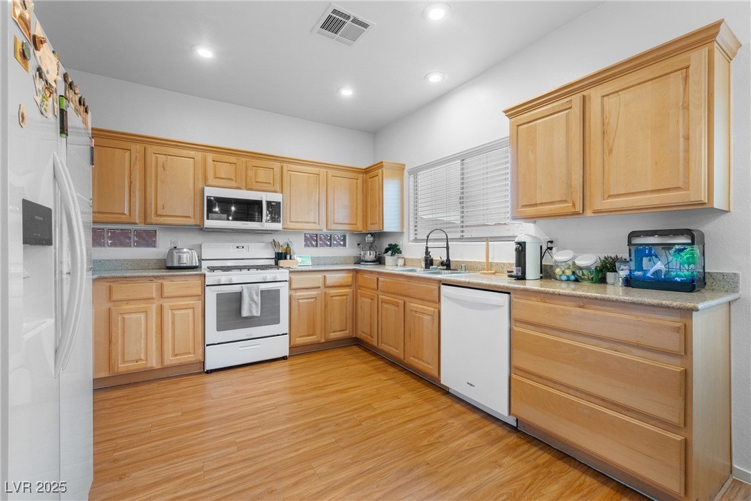 Kitchen with honey-colored cabinets, granite counters, white appliances, and wood-look flooring.