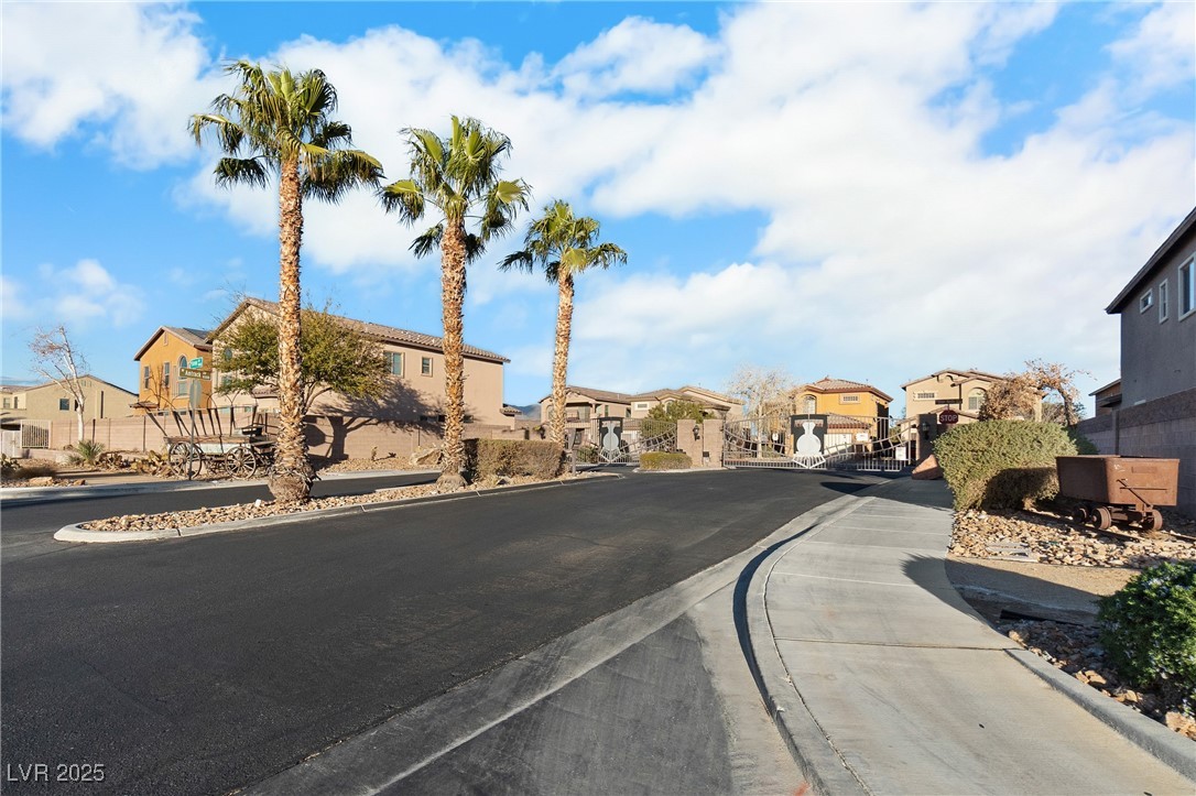 Gated residential community entrance with a curved street and three tall palm trees.