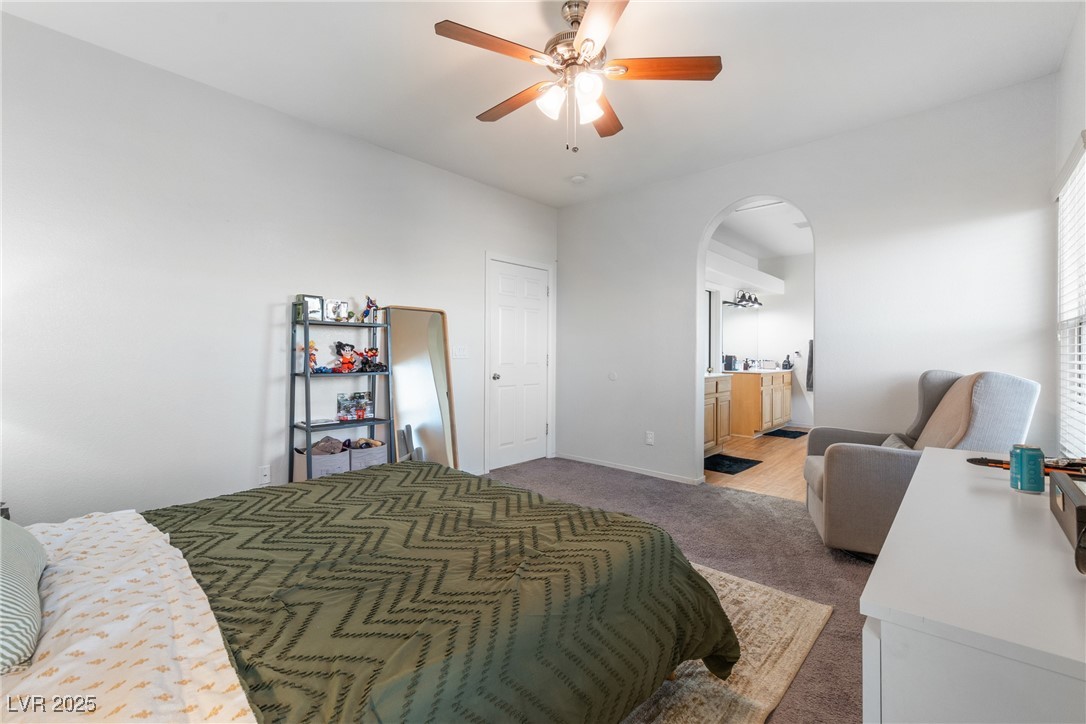 Bedroom with a green patterned bedspread, ceiling fan, and arched opening to a vanity area.