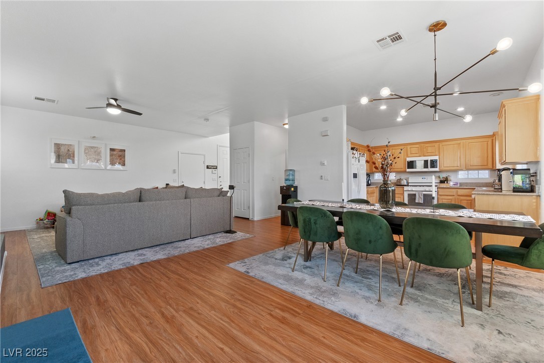 Open-plan living and dining area with a gray sectional, green chairs, and light wood kitchen cabinets.