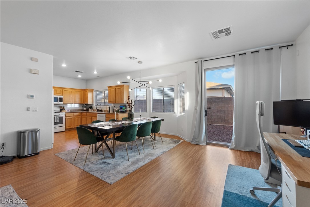 Open kitchen and dining area with warm wood cabinets, green dining chairs, and a curtained sliding glass door.