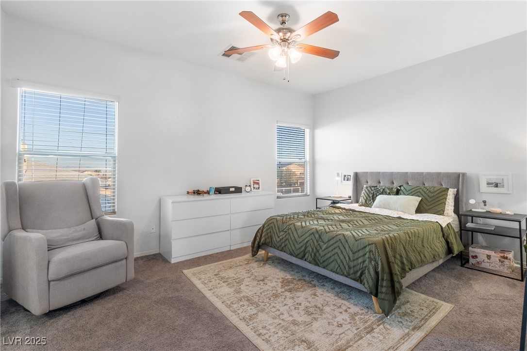 Bedroom with green bedding, two windows, a white dresser, and a gray armchair.