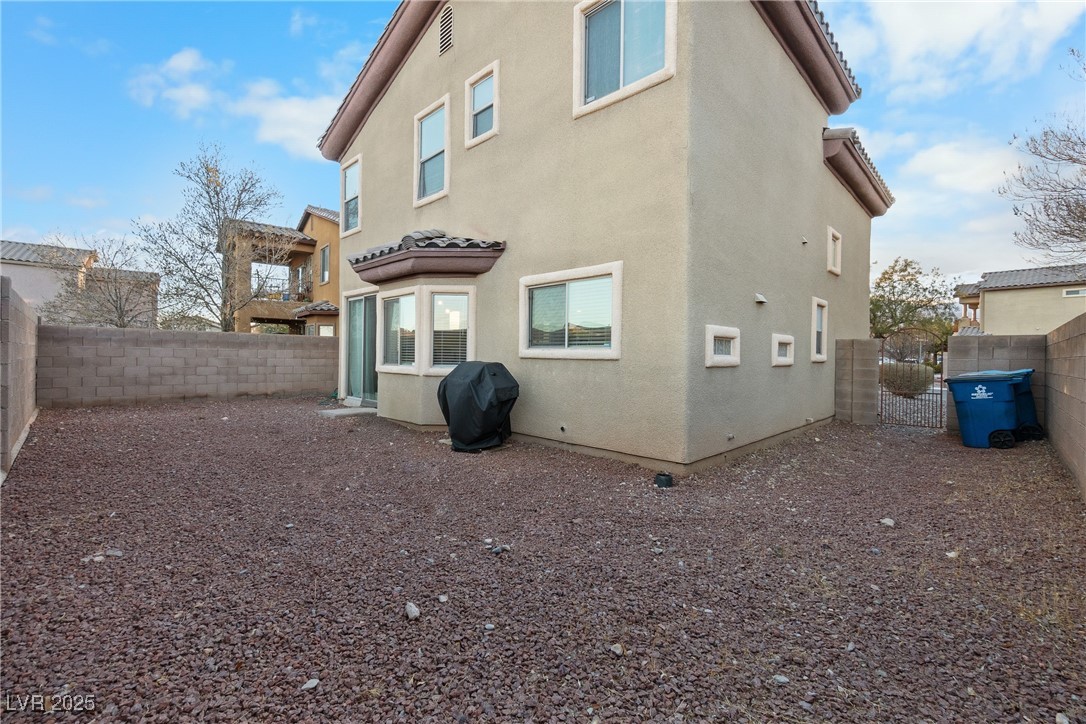 Two-story beige stucco home beside a gravel backyard enclosed by block walls.