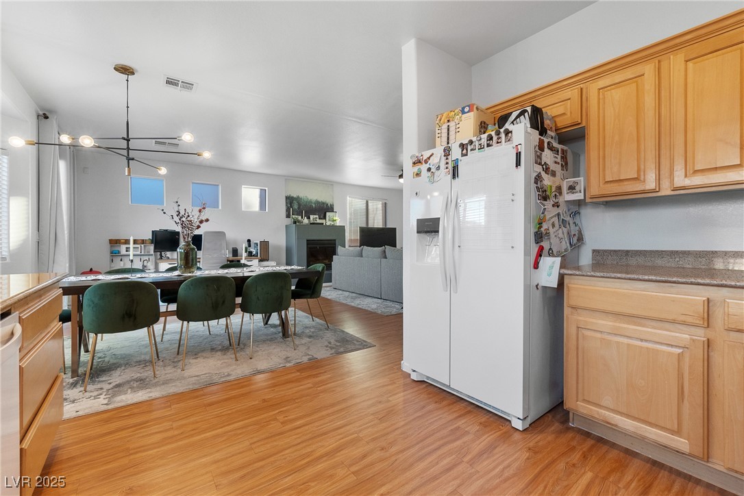 Open-plan kitchen and dining area with light wood cabinets, a white refrigerator, and hardwood floors.