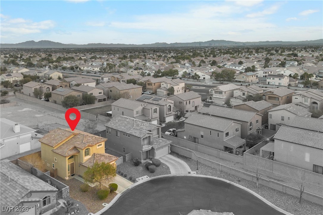 Aerial view of a tan two-story home highlighted among Las Vegas homes, with mountains beyond.