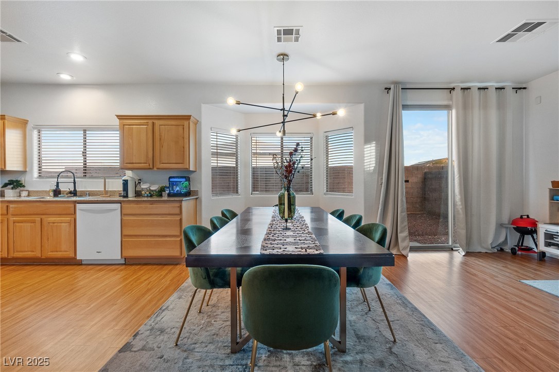 Dining area with a long dark table, green chairs, modern chandelier, and adjacent kitchen.
