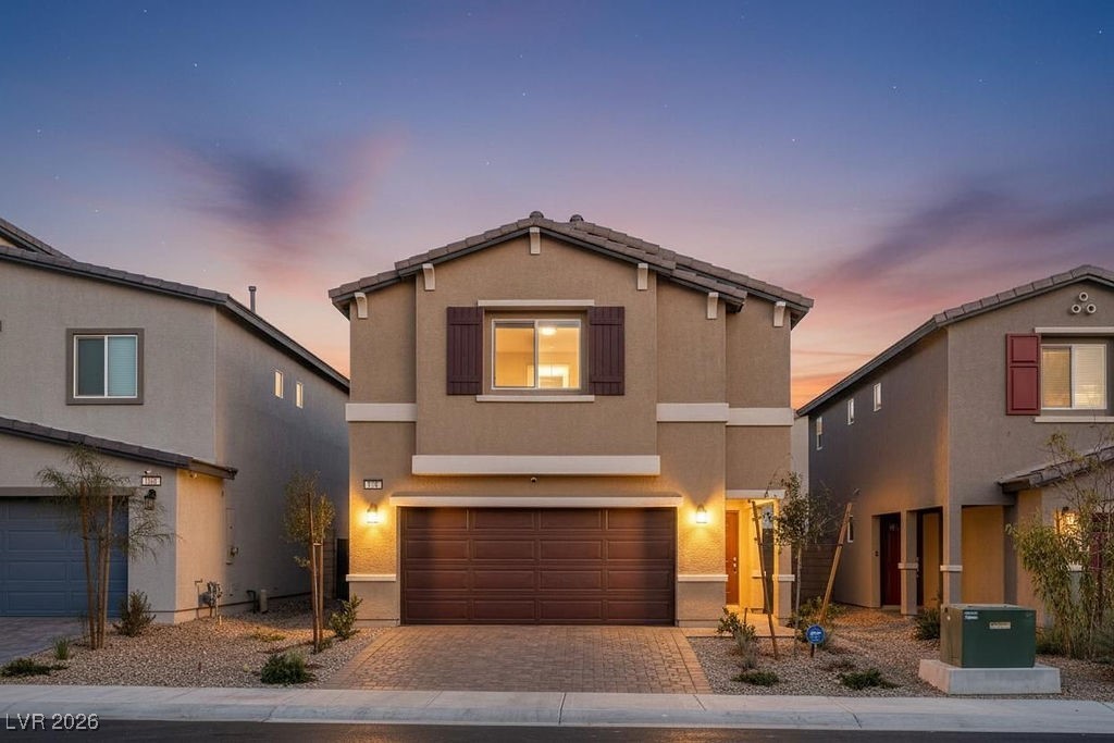 Two-story tan stucco home with a central garage and desert landscaping at dusk.