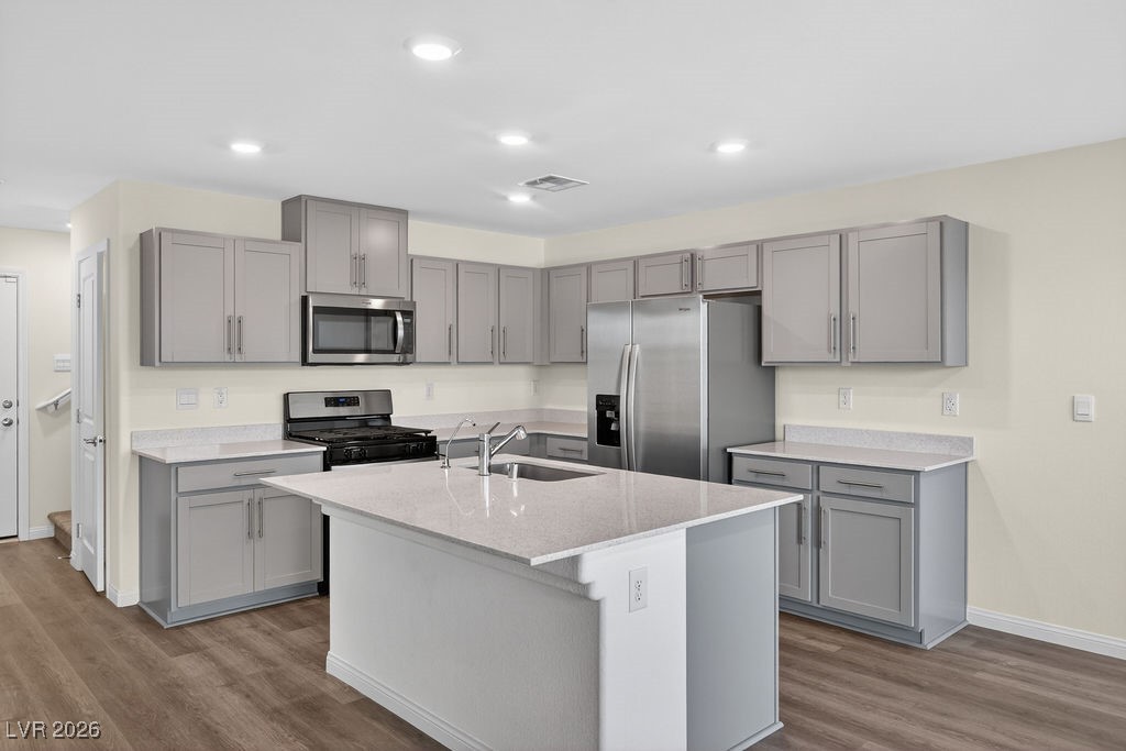 Kitchen with gray cabinets, stainless steel appliances, and a large island with a sink.
