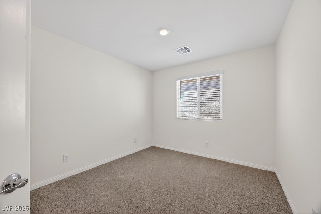 Empty bedroom with beige carpet and a window fitted with blinds.
