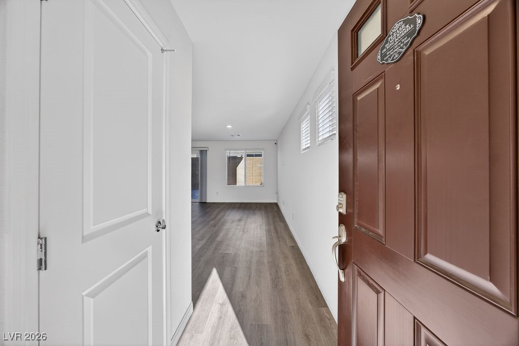 Entryway with a reddish-brown front door, gray wood-look flooring, and windows at the far end.