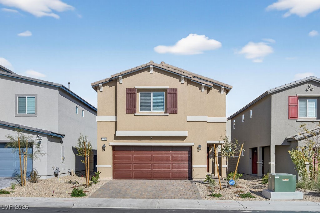 Two-story tan home with a red-brown double garage door and desert landscaping.