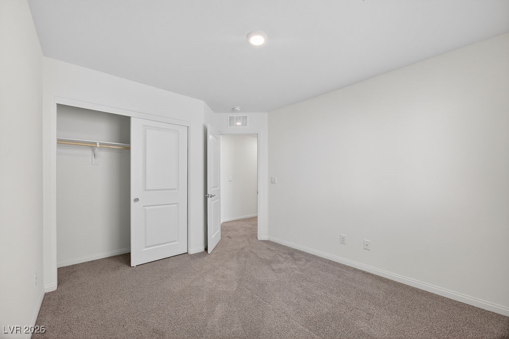Empty bedroom with beige carpet, an open closet, and a doorway to the hall.
