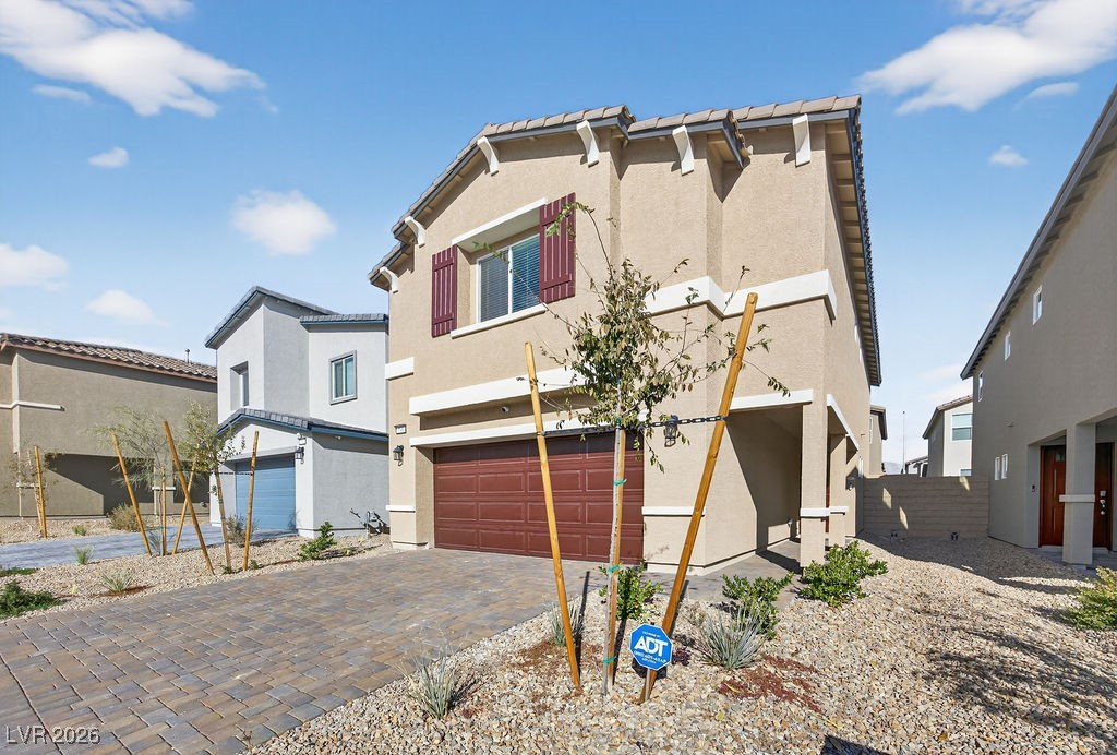 Two-story beige stucco home with burgundy shutters, a double garage, and a paved driveway.