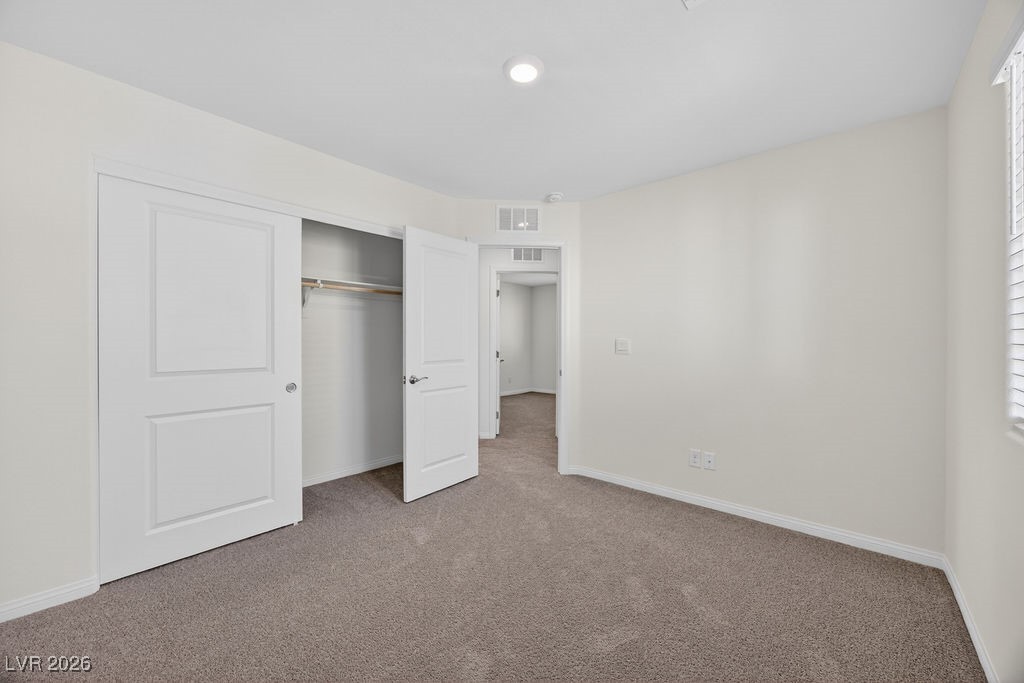 Empty bedroom with beige carpet, an open closet, and a doorway to the hall.